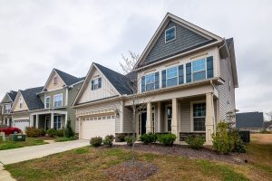 A row of modern suburban homes with garages, driveways, and landscaped lawns in daylight.
