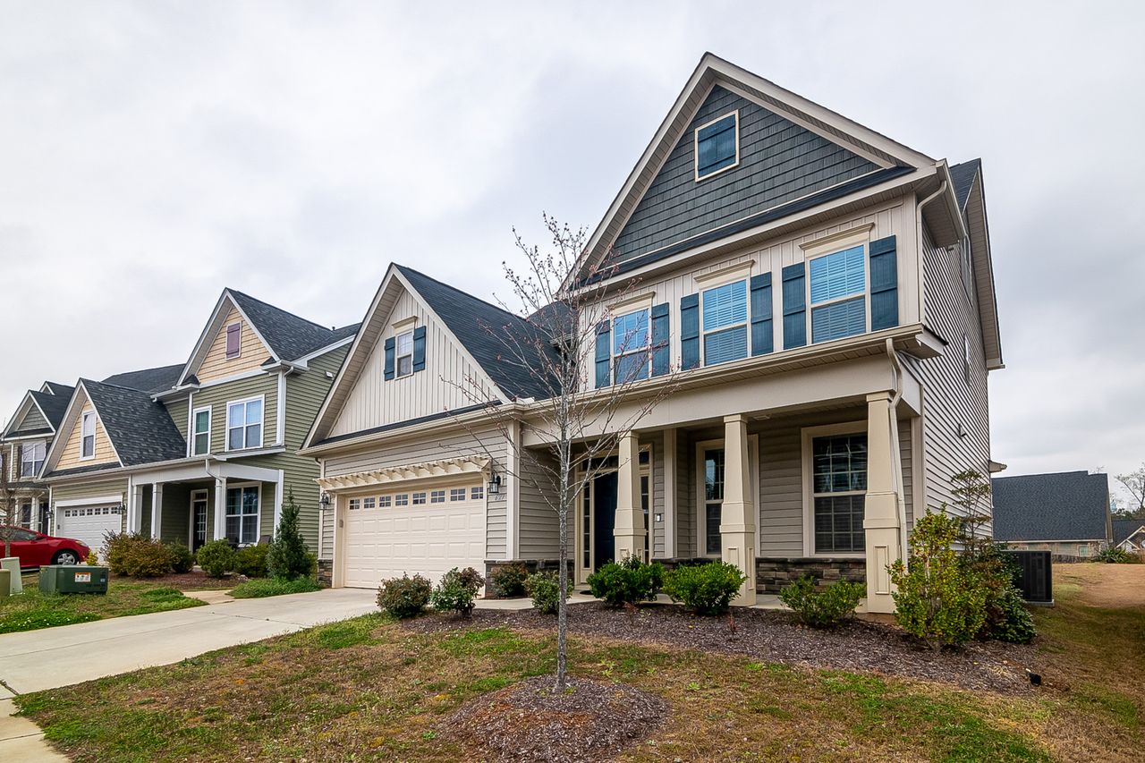 A row of modern suburban homes with garages, driveways, and landscaped lawns in daylight.
